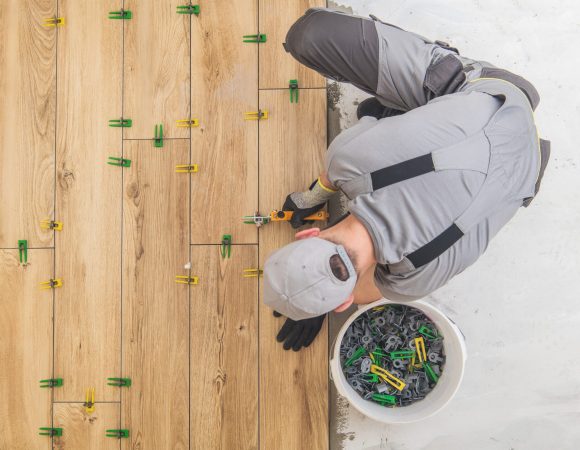 Ceramic Tiles Floor Installer. Wood Like Looking Tiles Installed by Professional Caucasian Construction Interior Finishing Worker. Flooring Industrial Theme.
