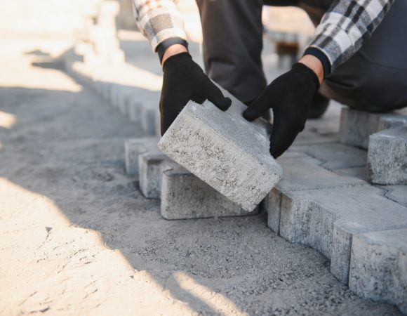 Close-up of construction worker installing and laying pavement stones on terrace, road or sidewalk. Worker using stones and rubber hammer to build stone sidewalk.